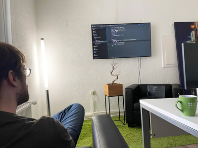 Moderner Arbeitsplatz mit Programmierer und Code auf Bildschirm Ein Programmierer sitzt in einem Büro, betrachtet einen Bildschirm mit Code. Im Vordergrund sind ein Tisch und eine Kaffeetasse zu sehen. Die Atmosphäre wirkt konzentriert und modern.